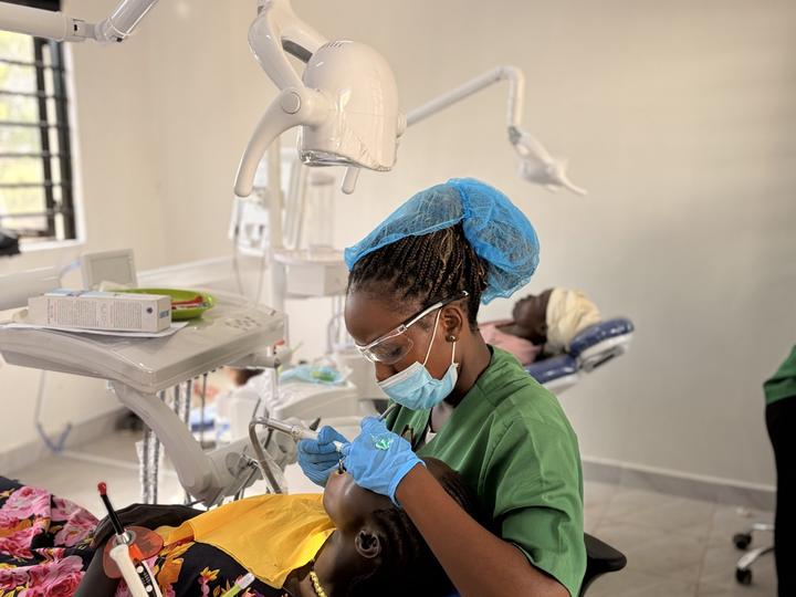 A Ugandan clinician in green scrubs treating a patient in a modern dental surgery