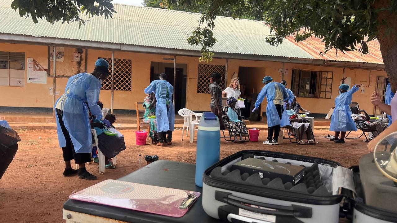 An outdoor dental clinic set up in front of a school building, with portable equipment and clinicians in blue gowns