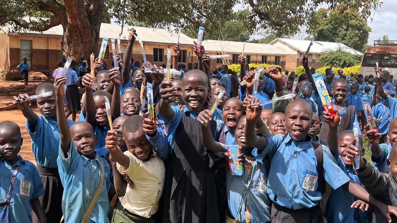 Schoolchildren in blue uniforms cheering and holding up new toothbrushes after an oral health session