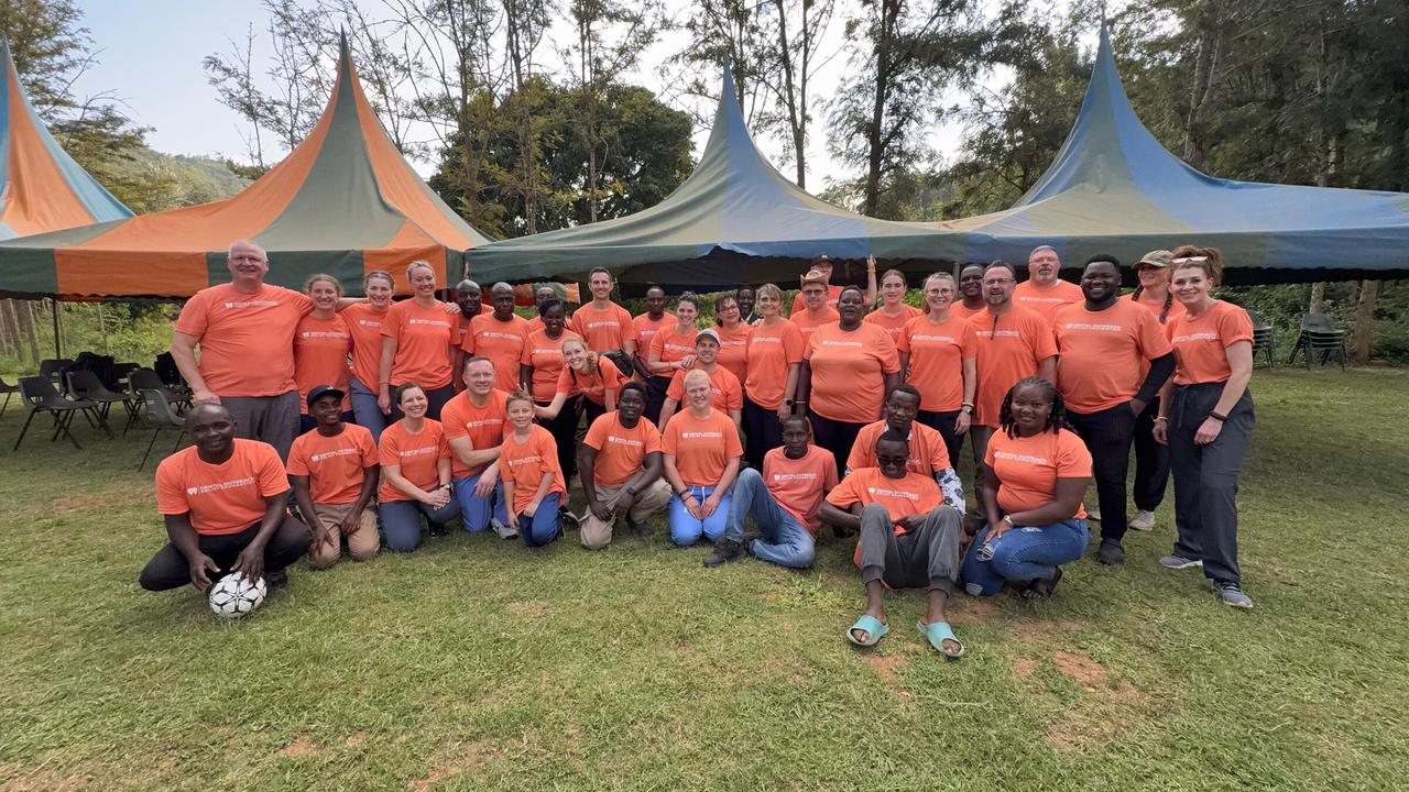 A large outreach team in matching orange shirts posing on the grass in front of tents