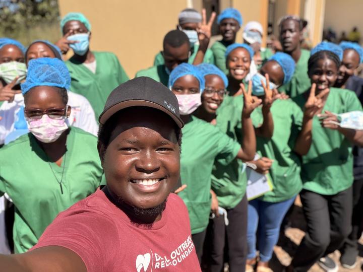 Smiling Ugandan healthcare students in green scrubs and caps taking a group selfie
